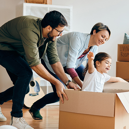 Happy parents having fun with their daughter while pushing her in carton box at their new home.